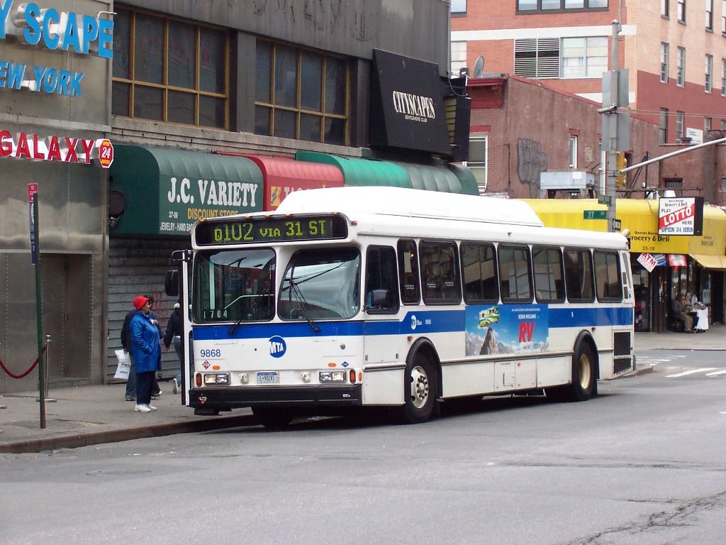 Passengers boarding a city bus on a busy street with buildings and traffic in the background.